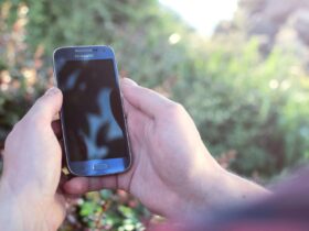 Mãos seguram um smartphone Samsung ao ar livre, com vegetação desfocada ao fundo.