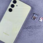 Smartphone ao lado de bandeja, cartão SIM e cartão de memória sobre uma superfície cinza.