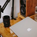 MacBook fechado sobre uma secretária de madeira, junto a equipamento de fotografia e som.