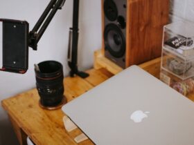 MacBook fechado sobre uma secretária de madeira, junto a equipamento de fotografia e som.
