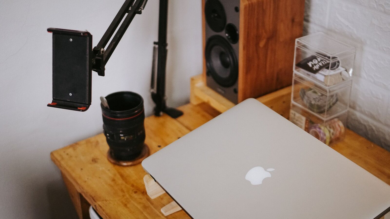 MacBook fechado sobre uma secretária de madeira, junto a equipamento de fotografia e som.