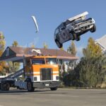 Automóvel deformado salta sobre um camião numa captura oficial de BeamNG.drive.