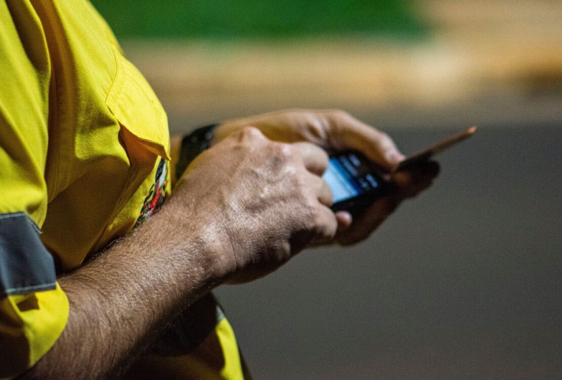 Pessoa com camisola amarela usa um smartphone à noite, com o fundo urbano desfocado.
