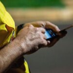 Pessoa com camisola amarela usa um smartphone à noite, com o fundo urbano desfocado.