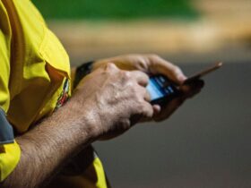 Pessoa com camisola amarela usa um smartphone à noite, com o fundo urbano desfocado.
