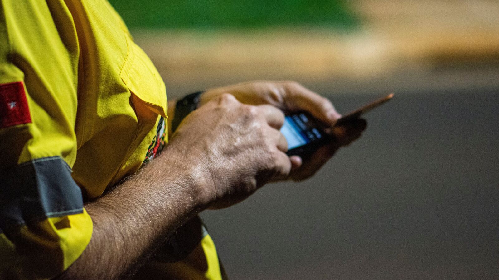 Pessoa com camisola amarela usa um smartphone à noite, com o fundo urbano desfocado.