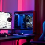 Computador gaming com monitor, auscultadores e cadeira iluminados por luzes azuis e vermelhas.