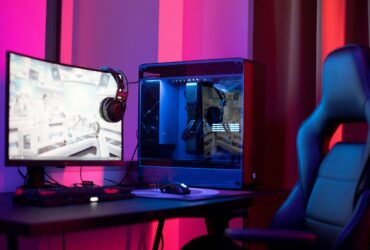 Computador gaming com monitor, auscultadores e cadeira iluminados por luzes azuis e vermelhas.