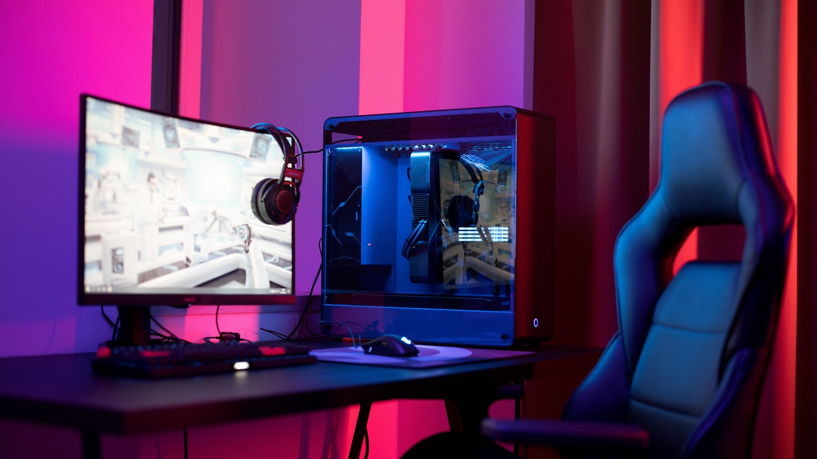 Computador gaming com monitor, auscultadores e cadeira iluminados por luzes azuis e vermelhas.