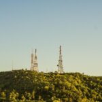 Torres de telecomunicações no alto de uma colina coberta por vegetação.
