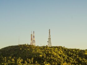 Torres de telecomunicações no alto de uma colina coberta por vegetação.