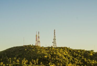 Torres de telecomunicações no alto de uma colina coberta por vegetação.