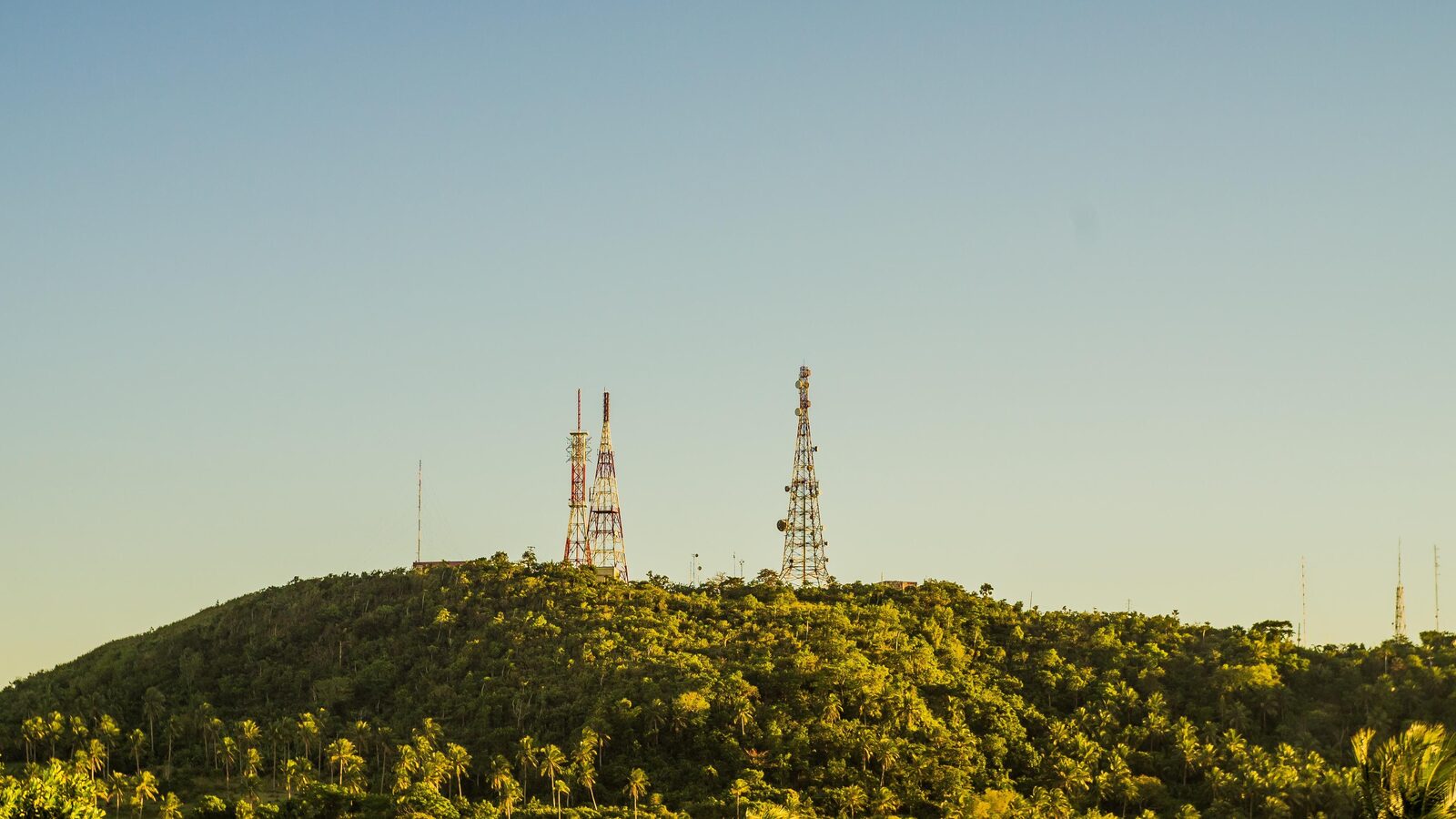 Torres de telecomunicações no alto de uma colina coberta por vegetação.