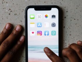 Mãos junto de um smartphone com ícones de aplicações, incluindo Facebook e Instagram, visíveis no ecrã.