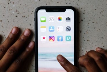 Mãos junto de um smartphone com ícones de aplicações, incluindo Facebook e Instagram, visíveis no ecrã.