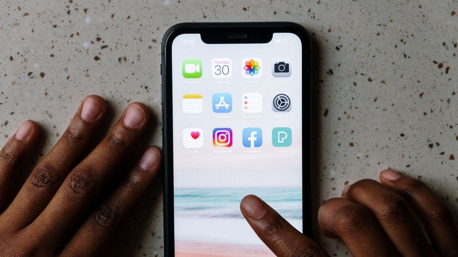 Mãos junto de um smartphone com ícones de aplicações, incluindo Facebook e Instagram, visíveis no ecrã.