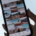 Mão segura um telemóvel que mostra uma grelha de fotografias no ecrã.