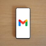 Telemóvel sobre uma mesa de madeira mostra o logótipo do Gmail no ecrã.