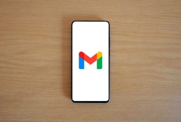 Telemóvel sobre uma mesa de madeira mostra o logótipo do Gmail no ecrã.
