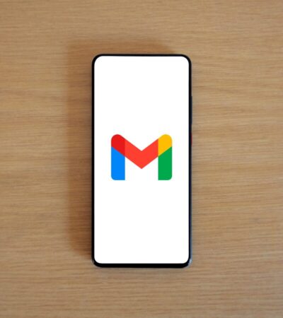 Telemóvel sobre uma mesa de madeira mostra o logótipo do Gmail no ecrã.