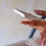 Pessoa segura um celular com a tela voltada para cima enquanto toca no aparelho em um ambiente interno.