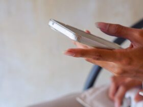 Pessoa segura um celular com a tela voltada para cima enquanto toca no aparelho em um ambiente interno.