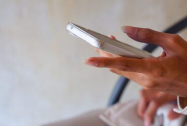 Pessoa segura um celular com a tela voltada para cima enquanto toca no aparelho em um ambiente interno.