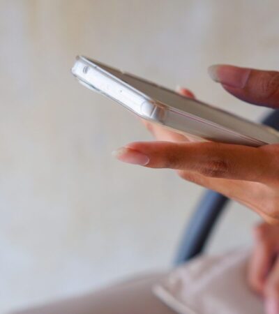 Pessoa segura um celular com a tela voltada para cima enquanto toca no aparelho em um ambiente interno.