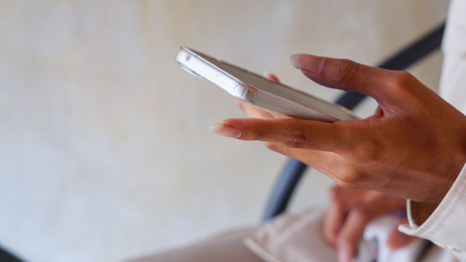 Pessoa segura um celular com a tela voltada para cima enquanto toca no aparelho em um ambiente interno.