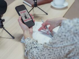 Pessoa segura um telemóvel junto a microfones e a um bloco de notas preparado para gravar um podcast.