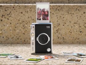 Câmara Instax Mini Evo 2 com uma fotografia a sair e várias impressões instantâneas dispostas à frente.
