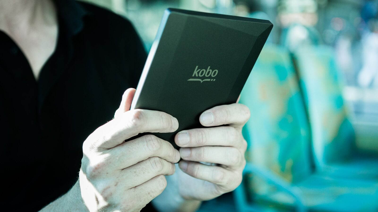 Pessoa segura um leitor digital Kobo durante uma viagem em transporte público.