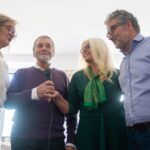 Quatro adultos participam numa sessão de karaoke com um microfone ao centro.