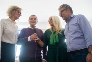 Quatro adultos participam numa sessão de karaoke com um microfone ao centro.