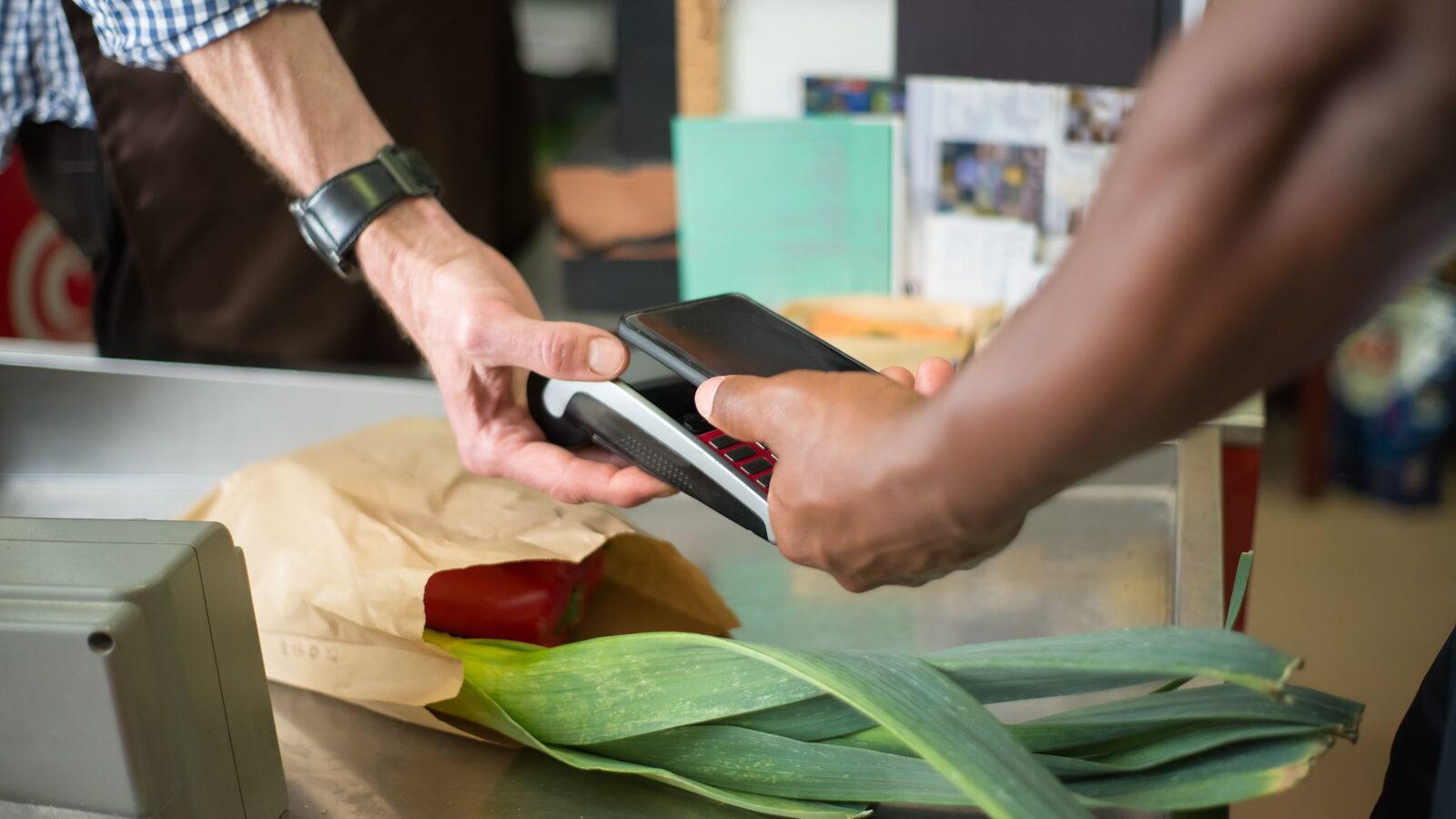 Pessoa aproxima um smartphone de um terminal de pagamento numa caixa de supermercado.