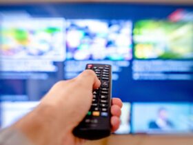 Mão aponta um comando para um televisor com o ecrã desfocado