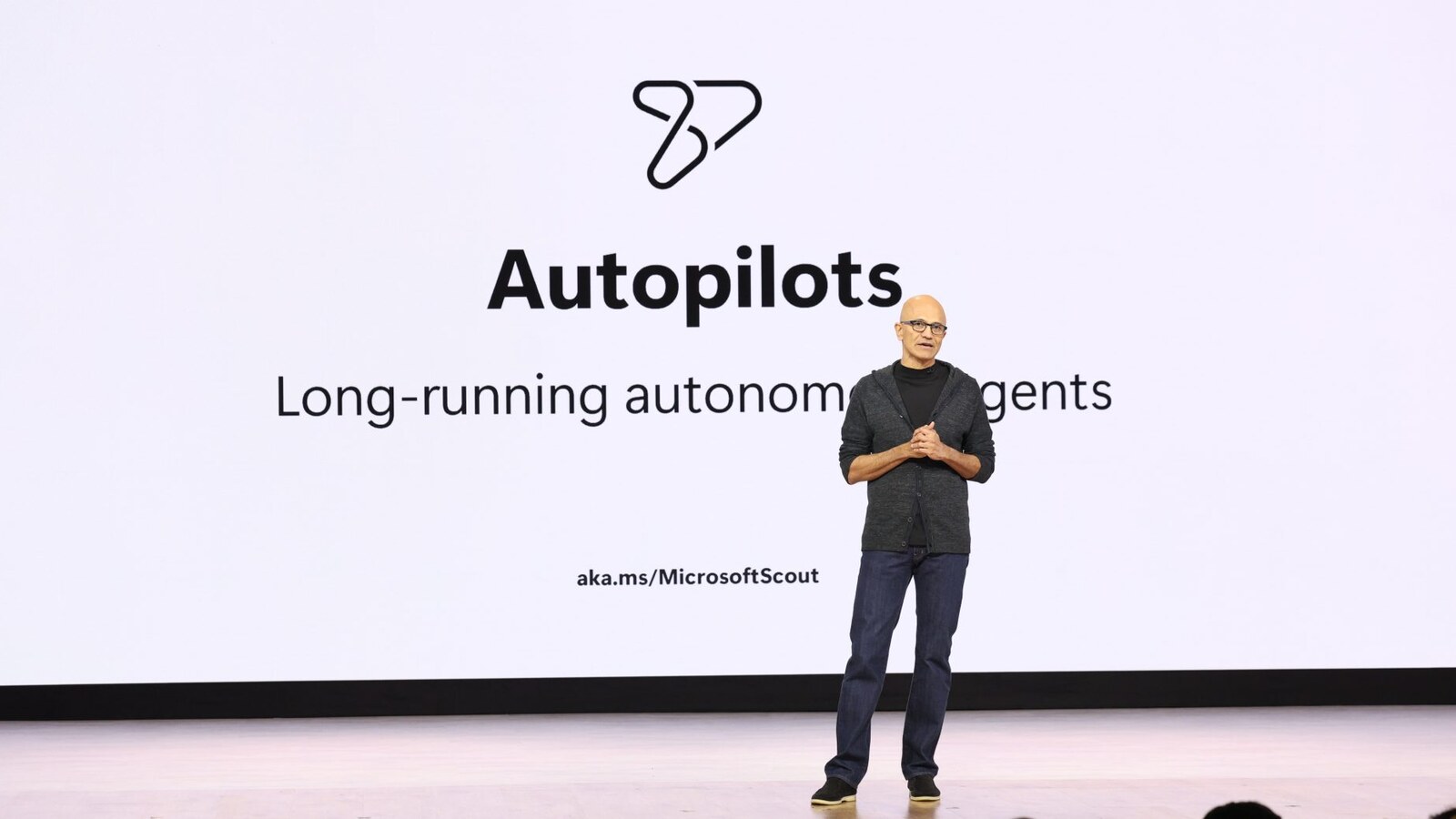 Satya Nadella fala no Microsoft Build 2026 diante de um slide sobre agentes autônomos de longa duração.