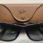Óculos Ray-Ban Meta pretos diante do respetivo estojo de carregamento castanho.