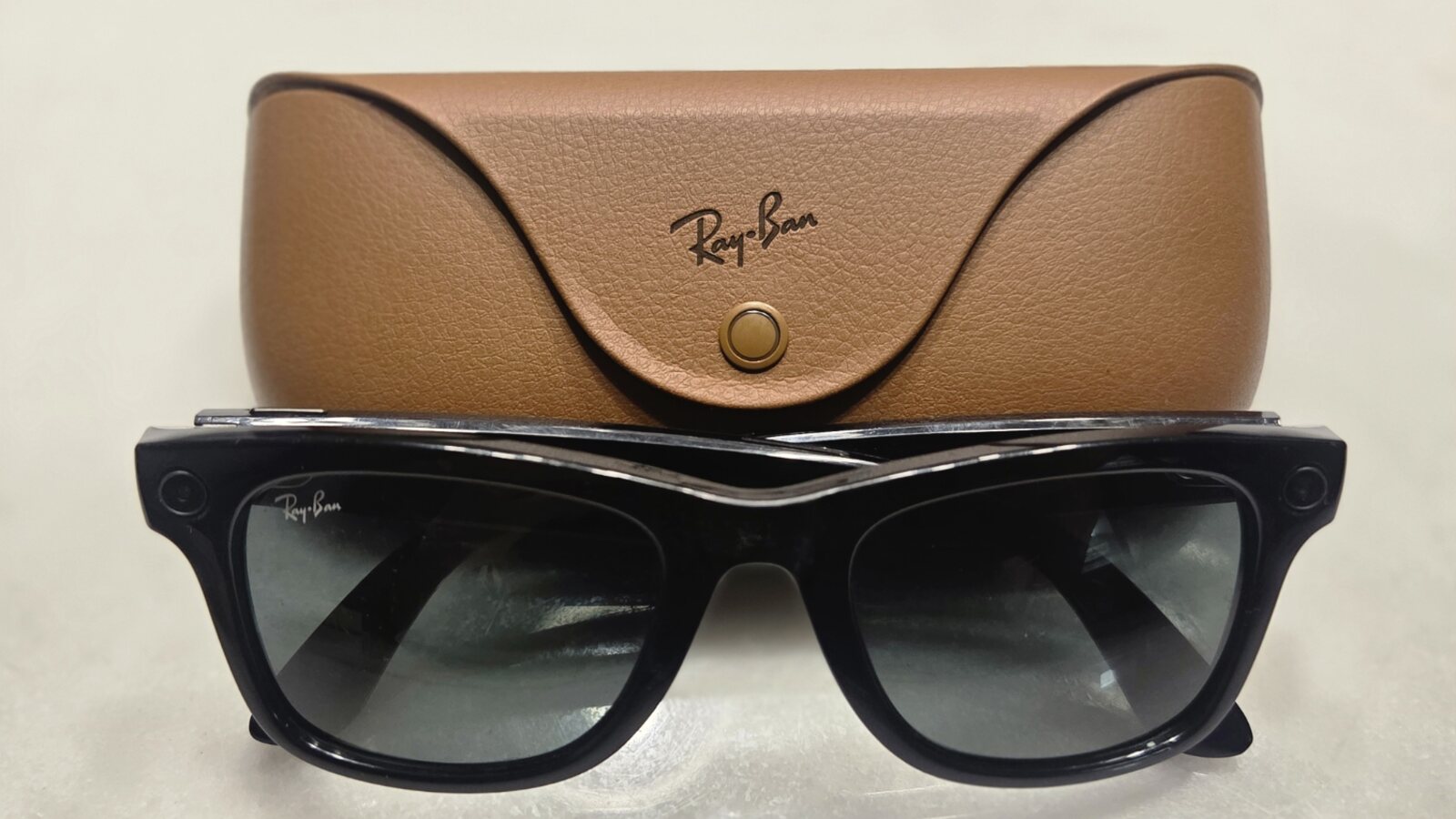 Óculos Ray-Ban Meta pretos diante do respetivo estojo de carregamento castanho.
