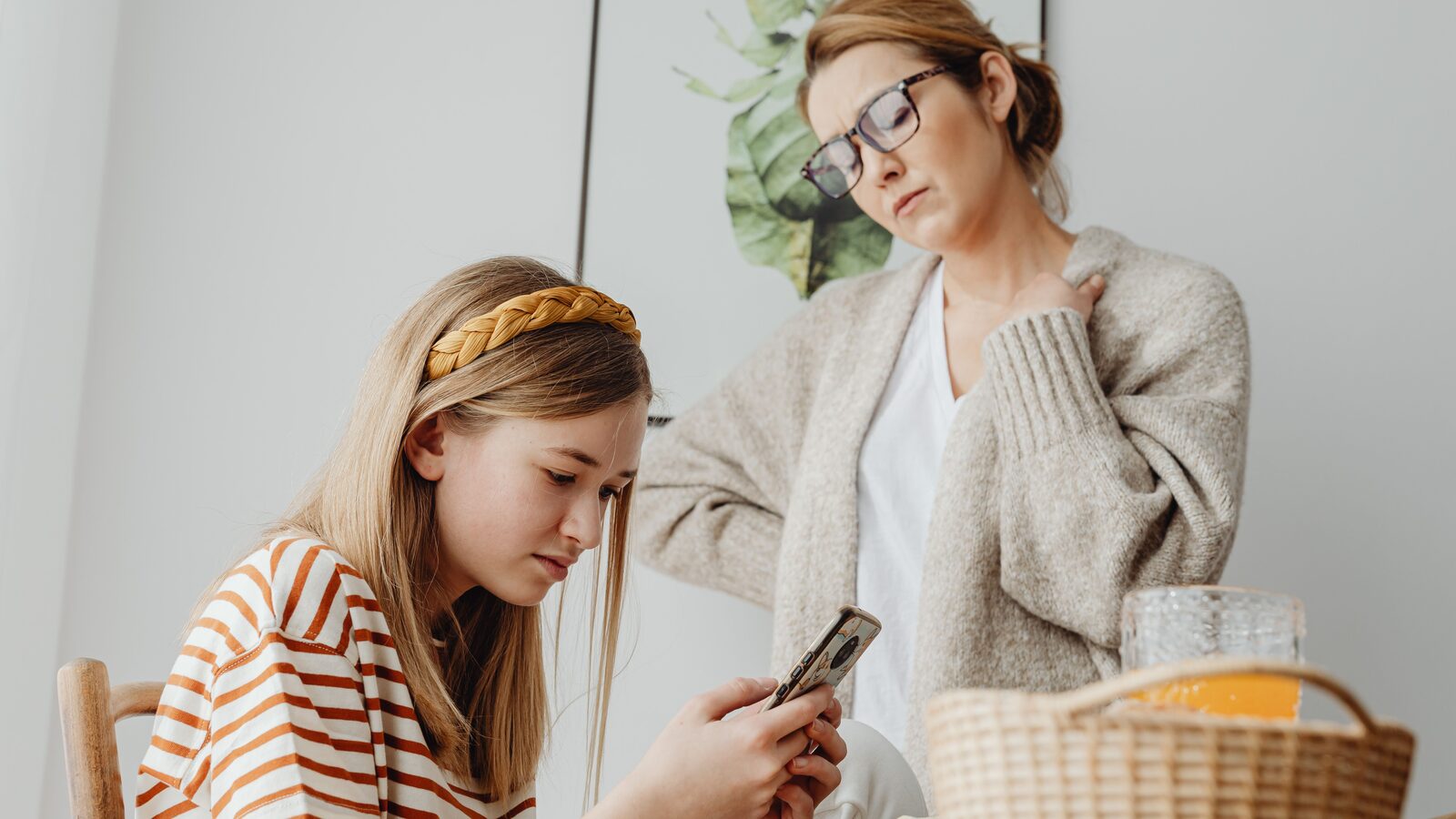 Mãe observa uma adolescente que usa um smartphone à mesa.