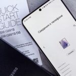 Smartphone Samsung no ecrã de informações do telefone, junto ao guia de início rápido e a uma capa preta