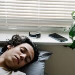 Pessoa a dormir junto a uma janela, com um smartwatch e um smartphone pousados no parapeito.