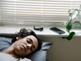 Pessoa a dormir junto a uma janela, com um smartwatch e um smartphone pousados no parapeito.