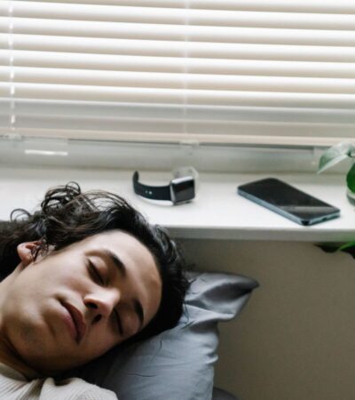 Pessoa a dormir junto a uma janela, com um smartwatch e um smartphone pousados no parapeito.