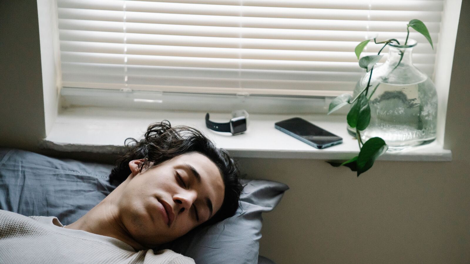 Pessoa a dormir junto a uma janela, com um smartwatch e um smartphone pousados no parapeito.