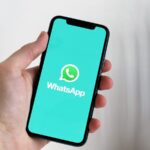Mão segura um smartphone com o logótipo do WhatsApp visível no ecrã.