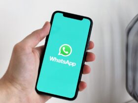 Mão segura um smartphone com o logótipo do WhatsApp visível no ecrã.