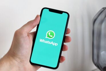 Mão segura um smartphone com o logótipo do WhatsApp visível no ecrã.