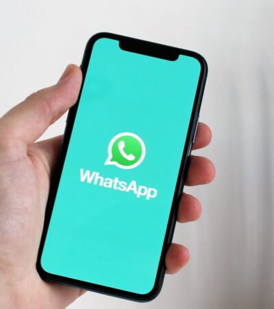 Mão segura um smartphone com o logótipo do WhatsApp visível no ecrã.