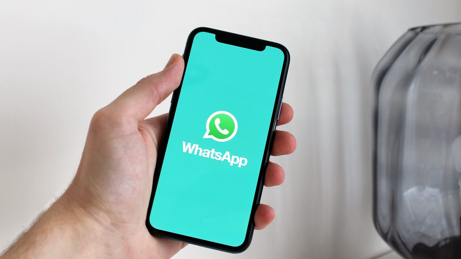 Mão segura um smartphone com o logótipo do WhatsApp visível no ecrã.